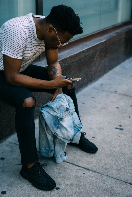 young black person sitting outside looking at phone