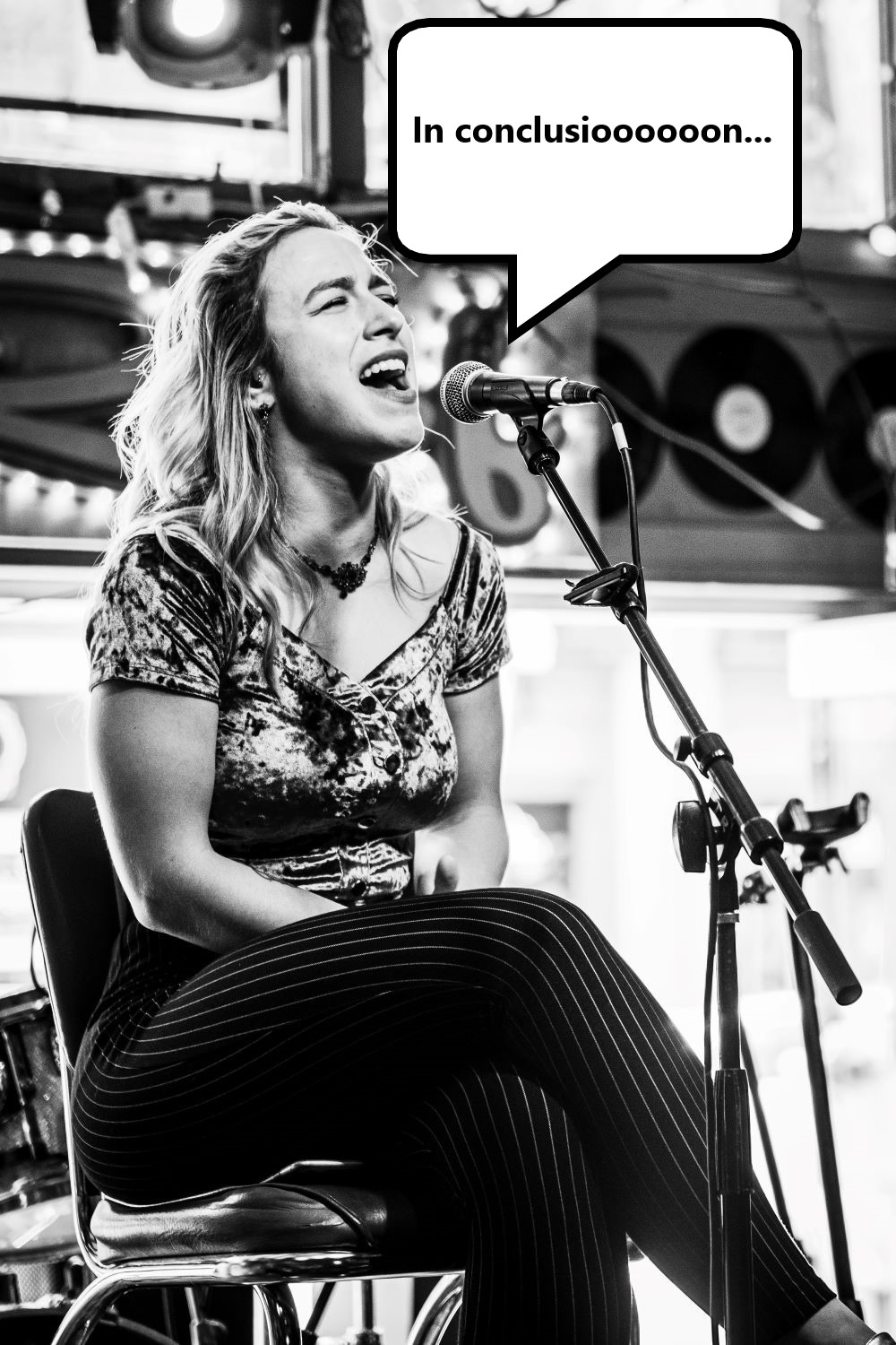 woman seated singing 'in conclusion' into microphone