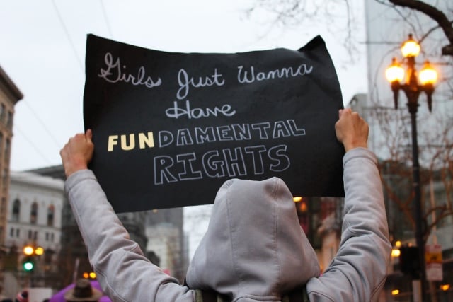 person in hoodie holding sign that says 'girls just wanna have fundamental rights'