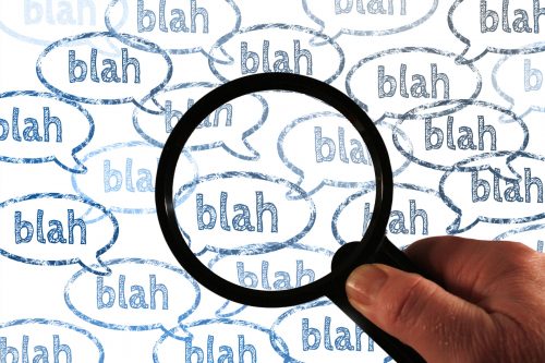 hand holding magnifying glass over speech bubbles containing the words 'blah blah blah'