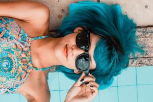 woman with blue hair lounging by pool in sunglasses