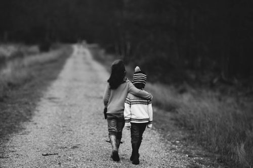 two siblings lovingly embracing while walking down a road