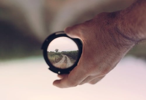 hand holding camera lens focused on a gravel road