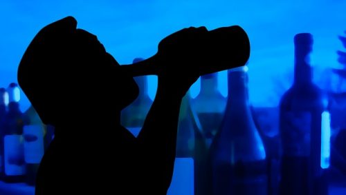 man drinking alcohol from bottle surrounded by other bottles
