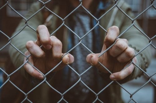 close up of hands gripping a fence in fear