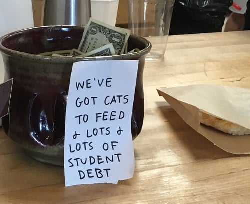 tip jar with note that says 'we've got cats to feed & lots of student debt'