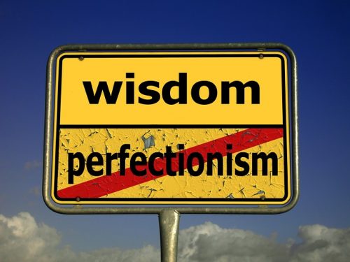 street sign with the word 'wisdom' over 'perfectionism' crossed out