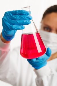 chemist observing beaker of red liquid