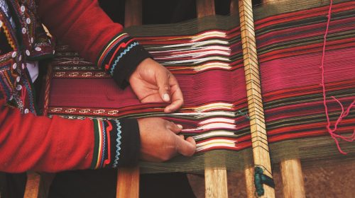 weaver's hands moving threads through loom