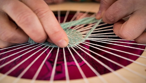 hands weaving blue thread in round loom