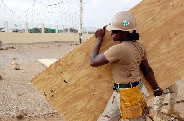 strong black woman carrying plywood on construction site