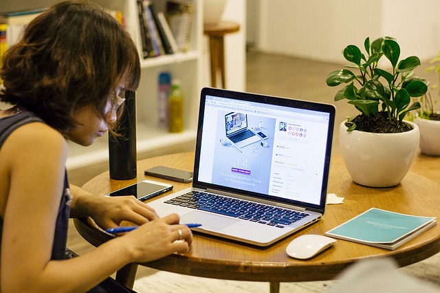 student writing on paper with open laptop